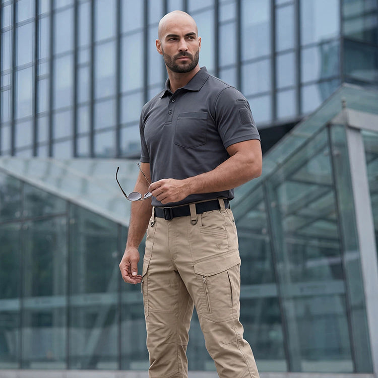 Man in khaki tactical pants and a gray polo standing outside a modern glass office building